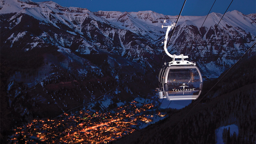 Riding the gondola in Telluride, Colorado at night with a mountain backdrop and city lights.