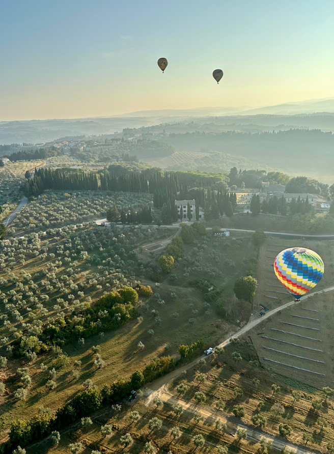 Sunrise image of hot air balloons floating over the Tuscan countryside.