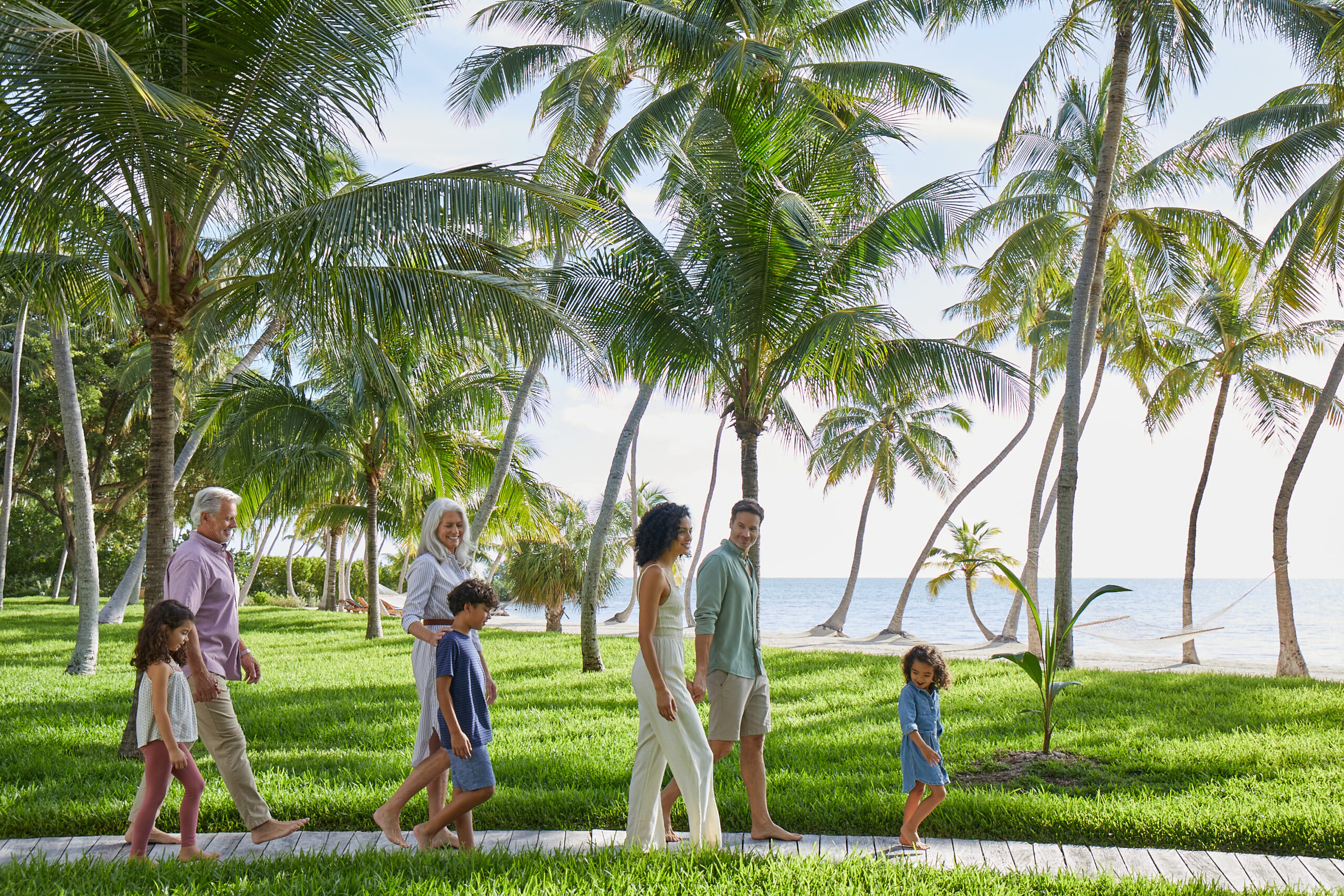 Grandparents and parents with three kids walking together on path to beach surrounded by palm trees in Florida Keys.