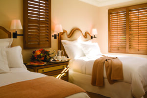 Double bedroom with white and camel bedding, wooden blinds at Pelican Hill Resort in Newport Coast.