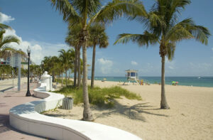 Sidewalk along sandy beach, palm trees and turquoise ocean waters in Fort Lauderdale, Florida.