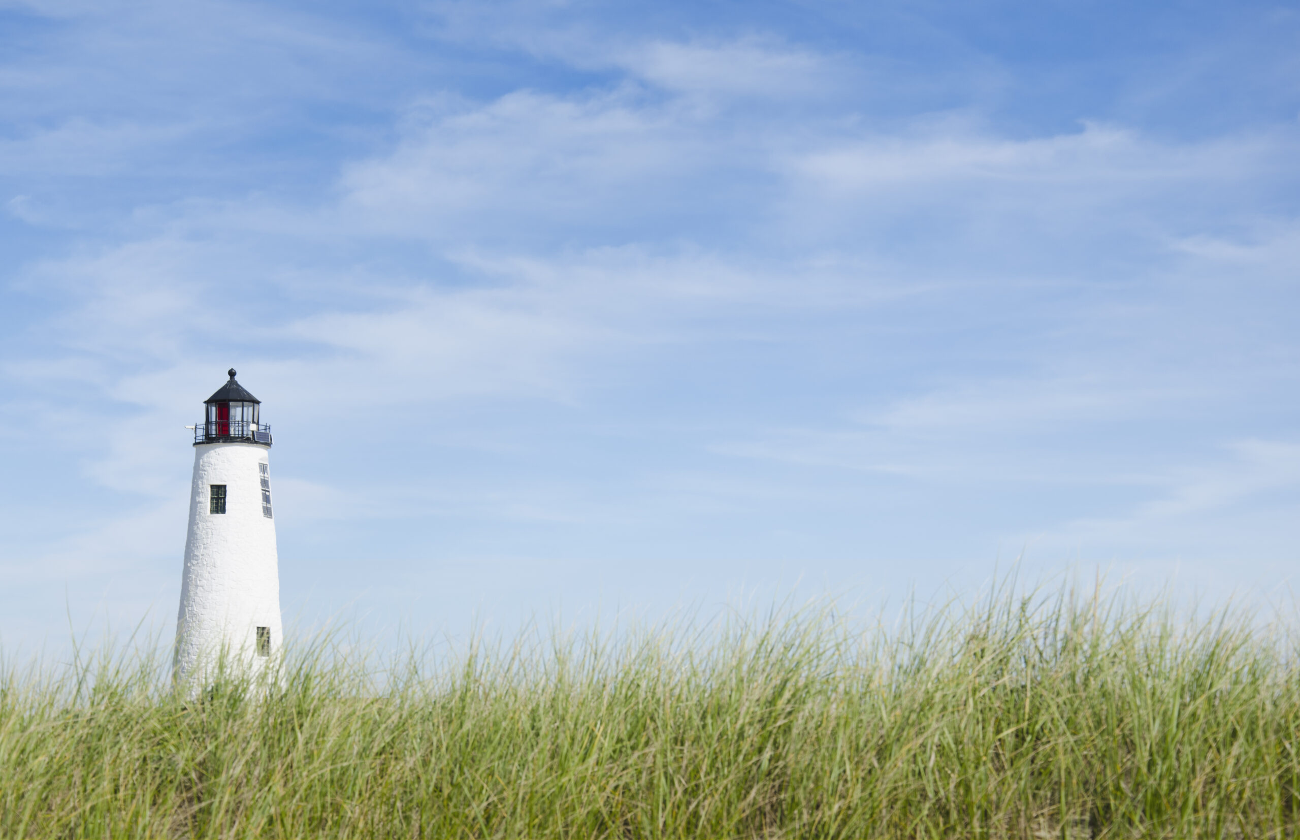 White light house in a field of wild grass with a baby blue sky.