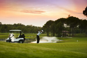 Golfer taking a swing at sunset on green golf course with pond and trees in Kiawah Island, South Carolina.