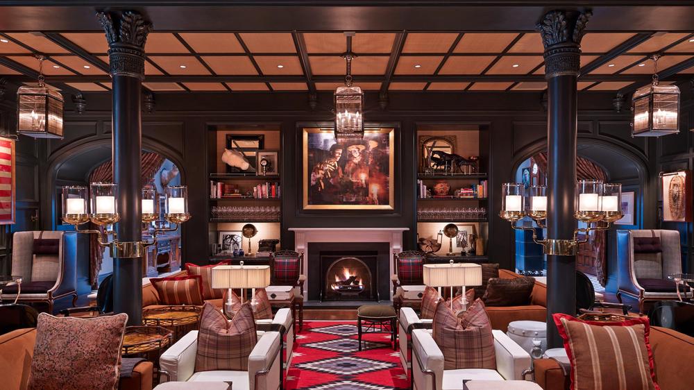 Cocktail lounge area of the Hotel Jerome with furniture arranged in small sitting area with fireplace with antique panting hanging above.