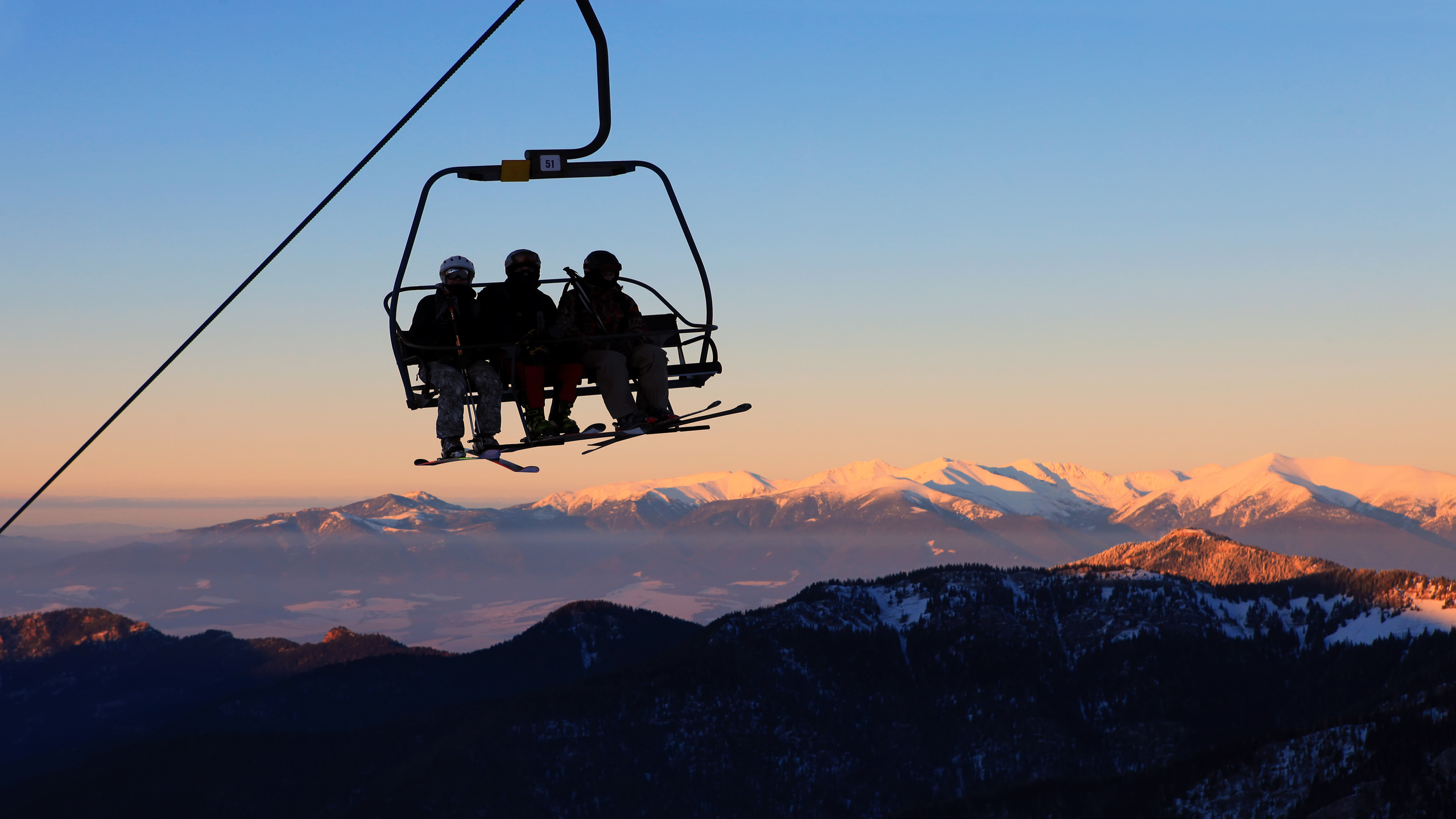 Silhouette of skiers on a chairlift with a mountain vista behind them during sunset