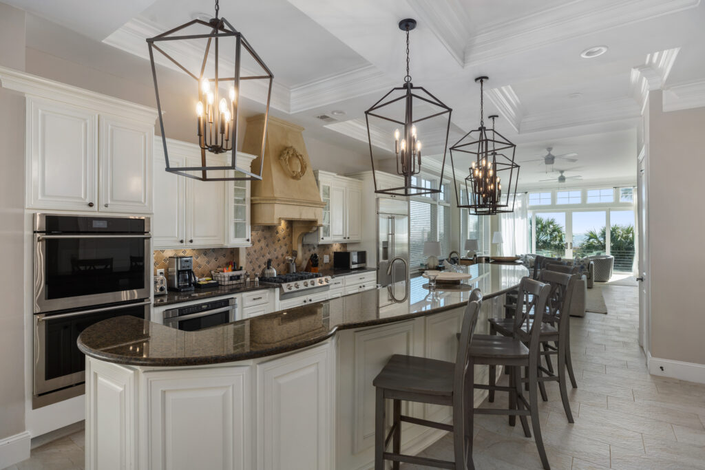 White kitchen with dark granite countertops, large island, and multiple chandeliers in Hilton Head Island, SC Inspirato home.