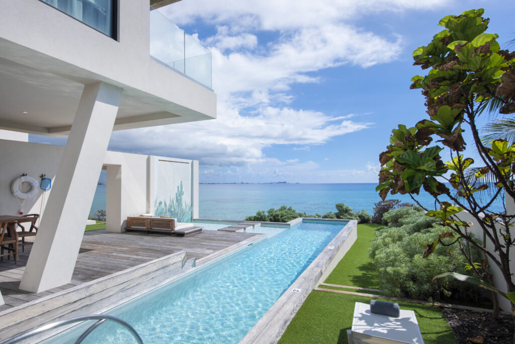 Private lap pool and outdoor patio overlooking the ocean at a white, modern Inspirato home in Grand Cayman, Cayman Islands.