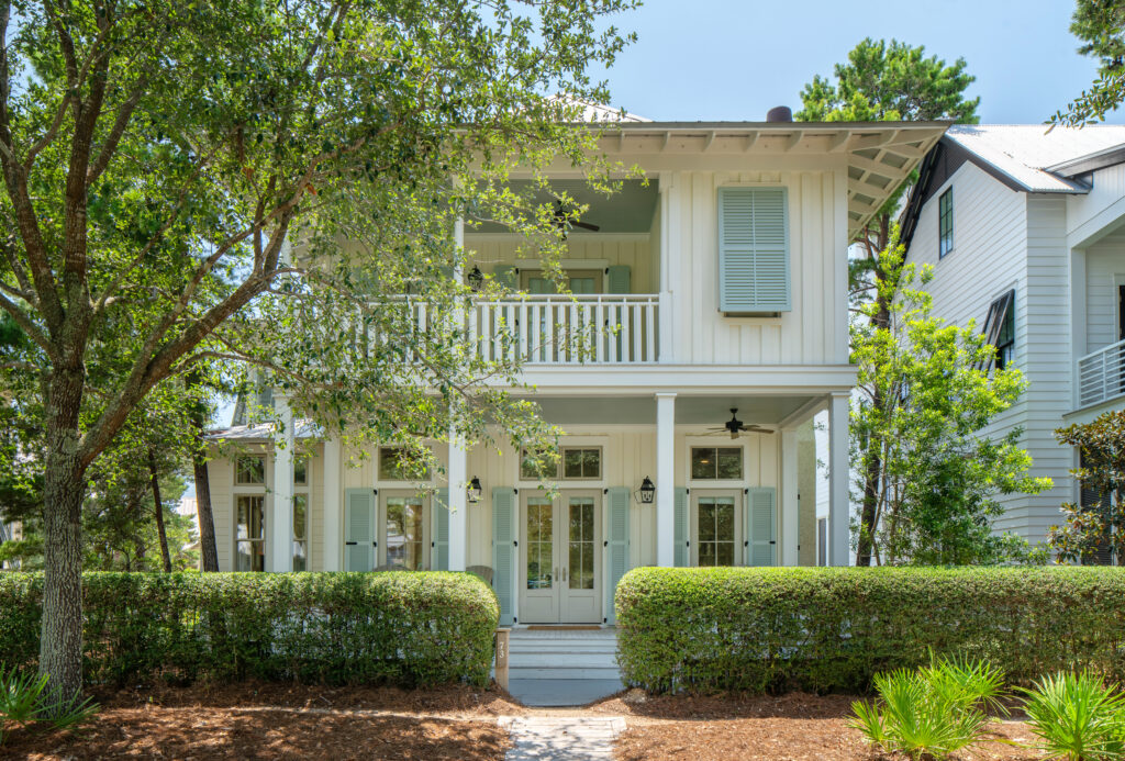 White and mint green front exterior of coastal Inspirato home in Rosemary Beach, Florida surrounded with green shrubs and trees.