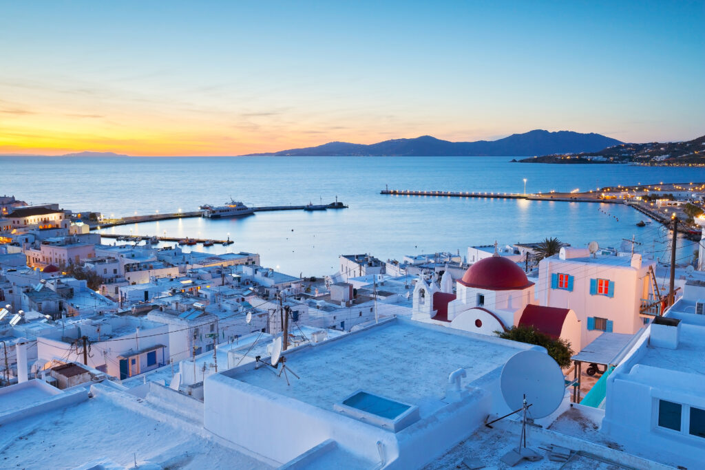 Whitewash buildings with blue shadow facing blue Mediterranean Sea at sunset in Mykonos, Greece.