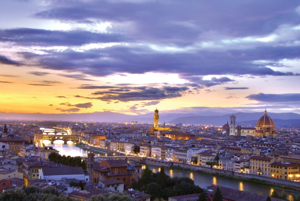 Aerial view of Florence, Italy lit up at night with fading orange and purple sunset.