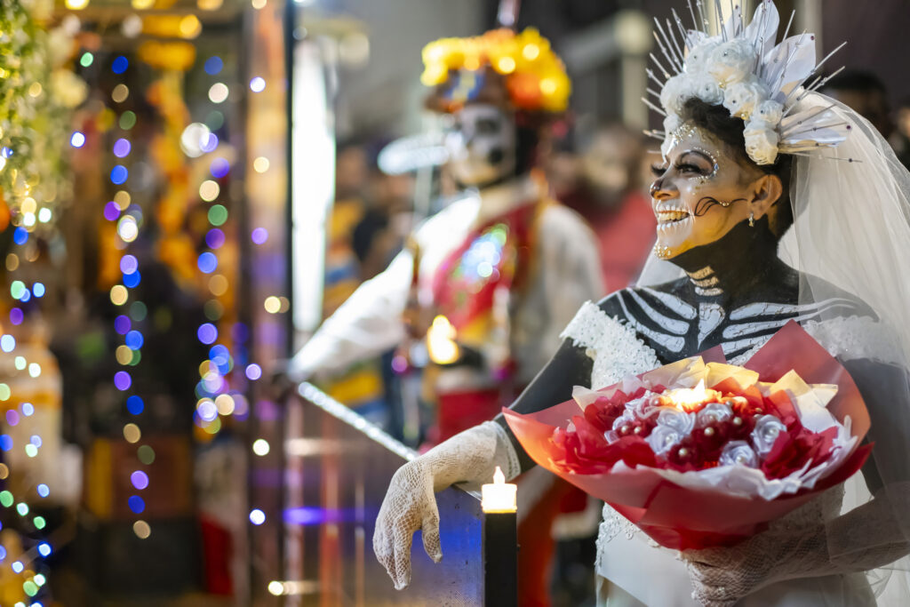 Women dressed up in Catrina makeup with a bouquet of flowers in her hand during a Día de los Muertos celebration.