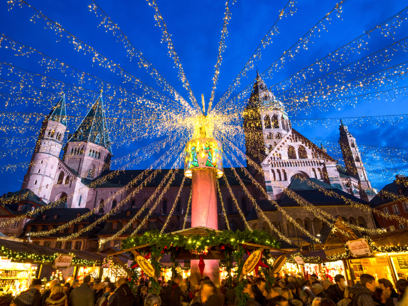 A European holiday market at night with strings of lights in front of a towering castle