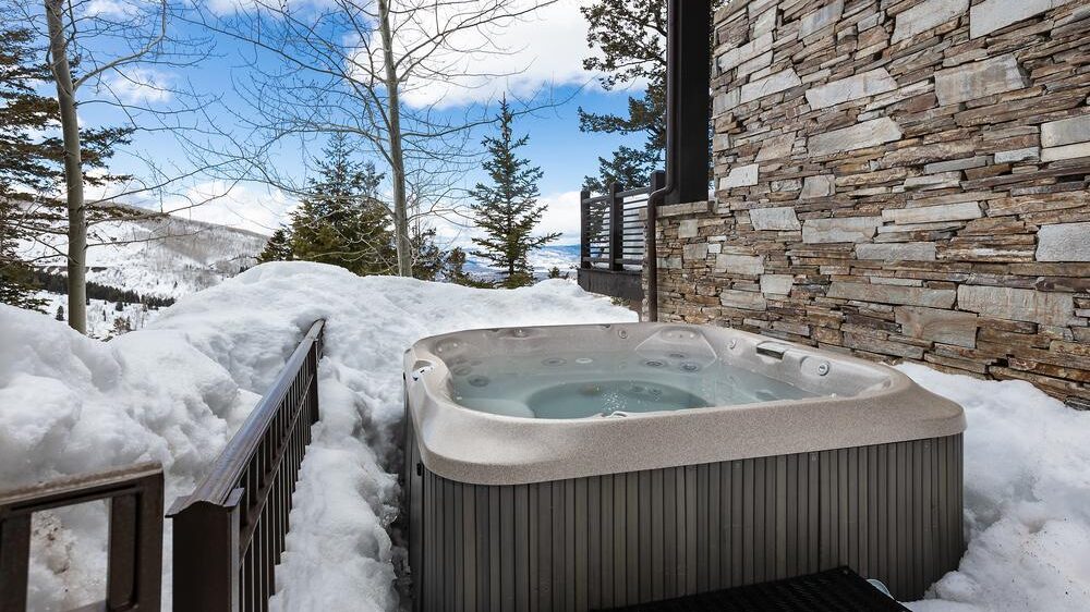 Royal Lookout hot tub area with the stone exterior or the home with snow pilled around the hot tub.