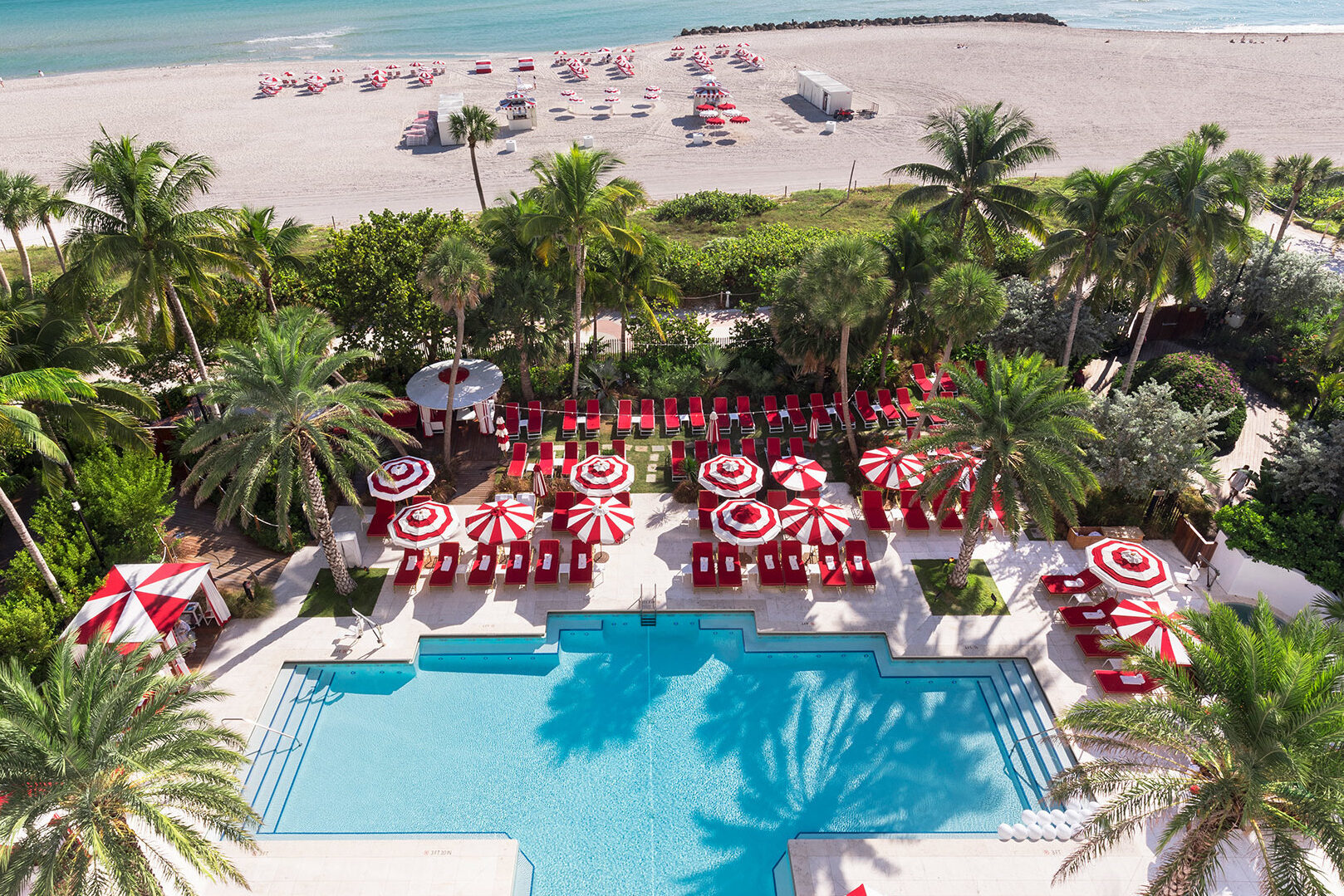 Faena Hotel Miami Beach pool area with the hotel beach behind and red and white umbrellas and chairs.