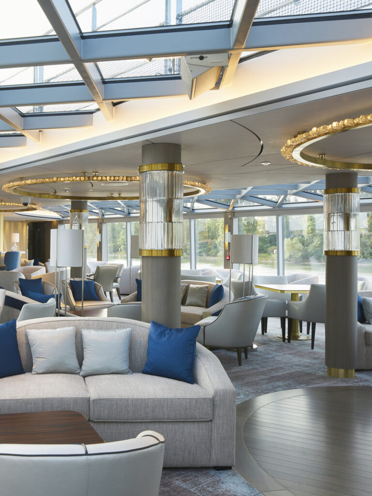 River cruise ship lounge area with glass ceiling and lots of furniture arrange in circles.