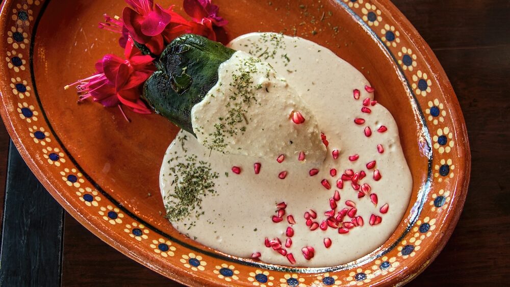 Chiles en nogada dish of poblano peppers filled with a sauce garnished with pomegranate seeds on some traditional Mexican dishware.