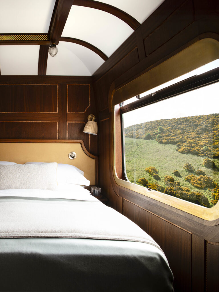 Cozy and luxurious train suite with a plush bed and scenic countryside views through a large picture window.