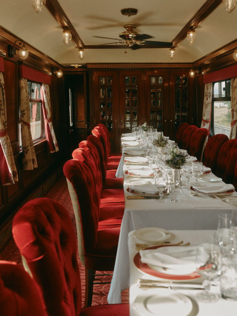 Elegant dining car aboard the Belmond Royal Scotsman, featuring white tablecloths, crystal glassware, and plush red velvet chairs.