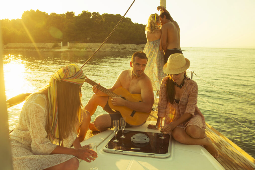Group of friends enjoying sunset champagne and live guitar music aboard a private yacht, capturing the carefree luxury and curated experiences of an Inspirato sailing vacation.