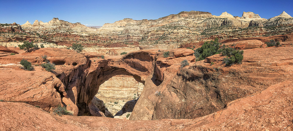 Natural sandstone arch surrounded by layered red and white rock formations in Capitol Reef National Park under a clear blue sky.