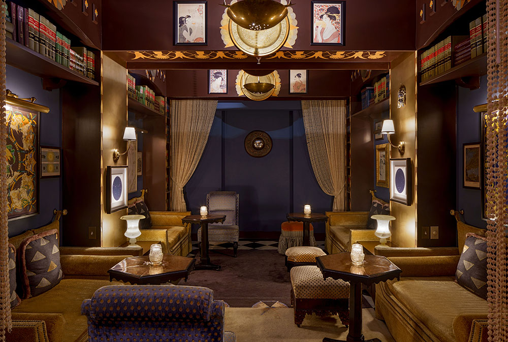 Elegant speakeasy lounge at Maison Métier in New Orleans featuring plush vintage seating, moody lighting, art deco details, and curated bookshelves.