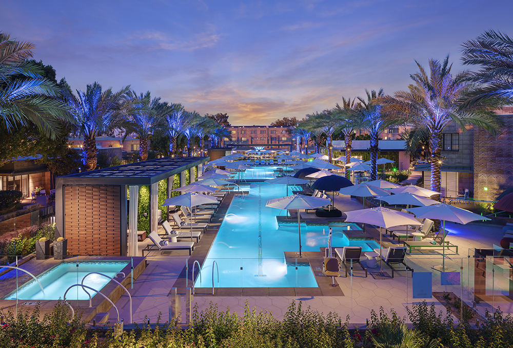 Twilight view of Saguaro Pool at Arizona Biltmore, lined with palm trees, cabanas, and loungers for a glamorous desert escape.