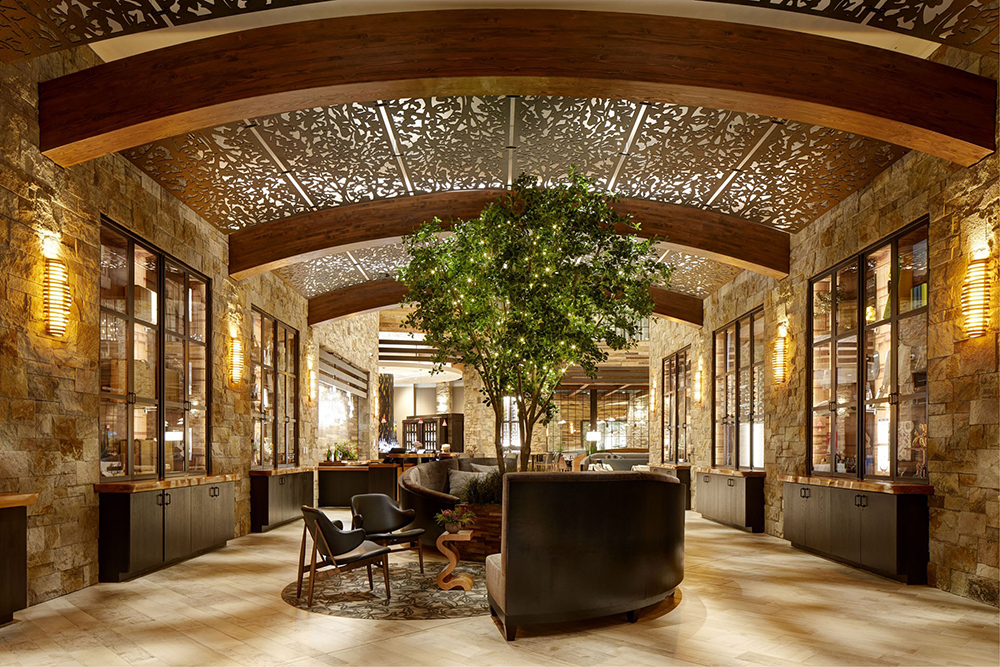 Sophisticated hotel lobby with stone walls, sculpted wood beams, and a tree adorned with twinkle lights—welcoming entrance to Archer Hotel Napa, part of the Inspirato Collection