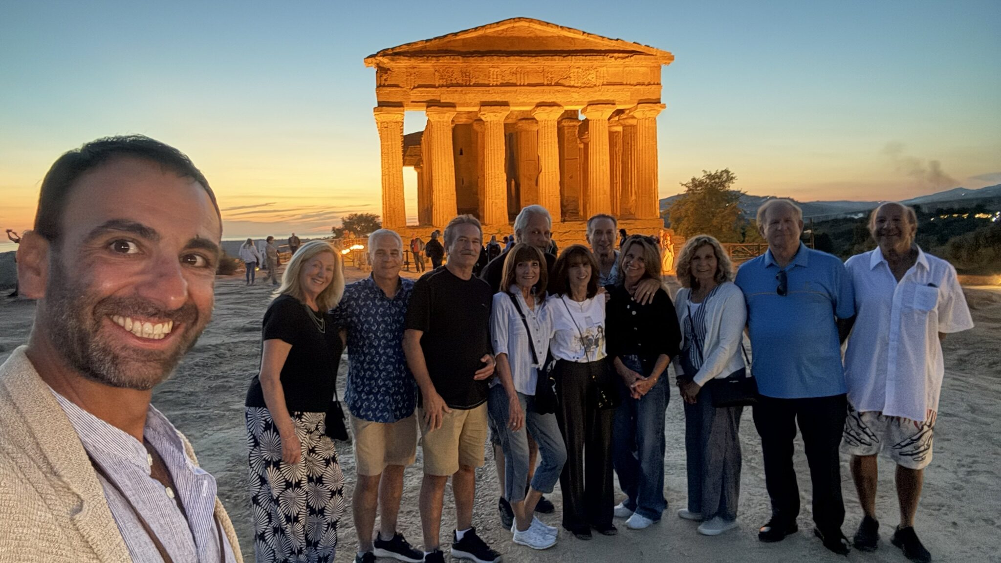 Group photo at sunset in front of the illuminated Temple of Concordia in the Valley of the Temples, Agrigento, Sicily. The group stands smiling with their tour guide, capturing a memorable moment during their bespoke family trip across the island.