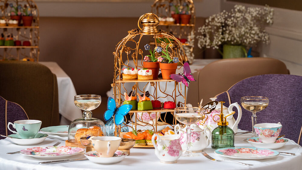 Elegant afternoon tea setting at Kona Restaurant in London, featuring tiered pastries, floral china, champagne coupes, and whimsical garden-inspired details.