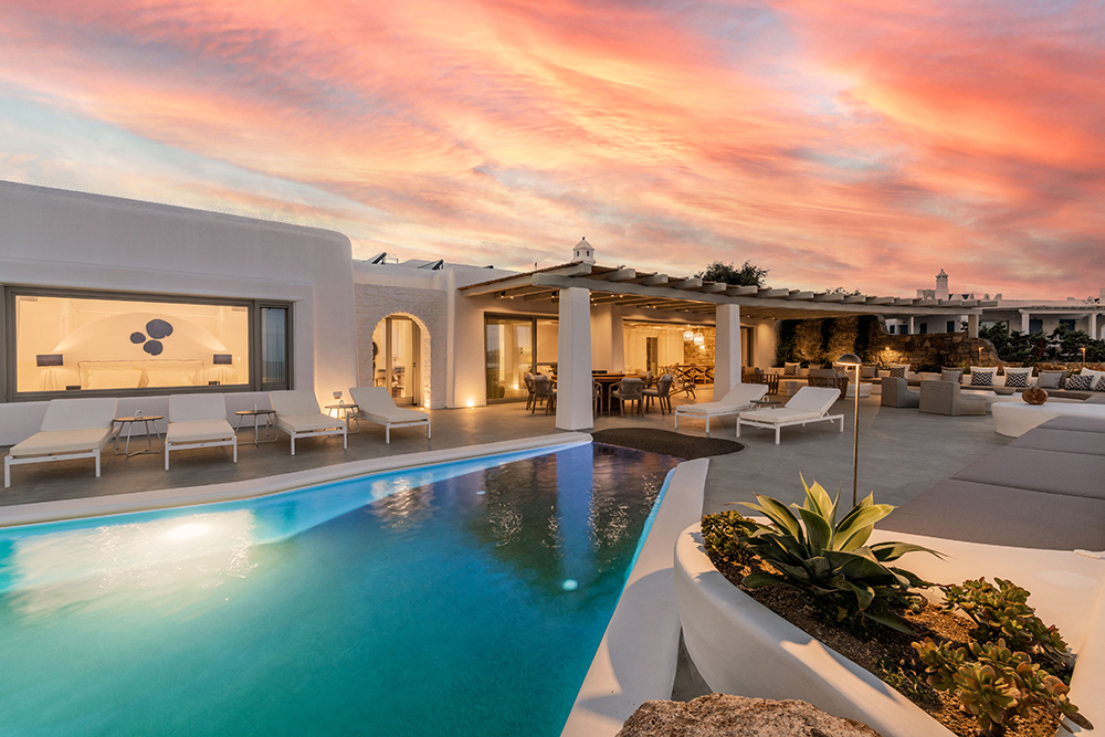 Sunset view of a luxury Mykonos villa featuring private pool, Cycladic architecture, and ambient lighting for evening relaxation.