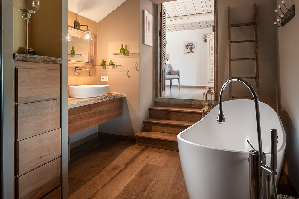Warm-toned bathroom in a Provence villa featuring a freestanding bathtub, rustic wooden floors, and natural finishes.