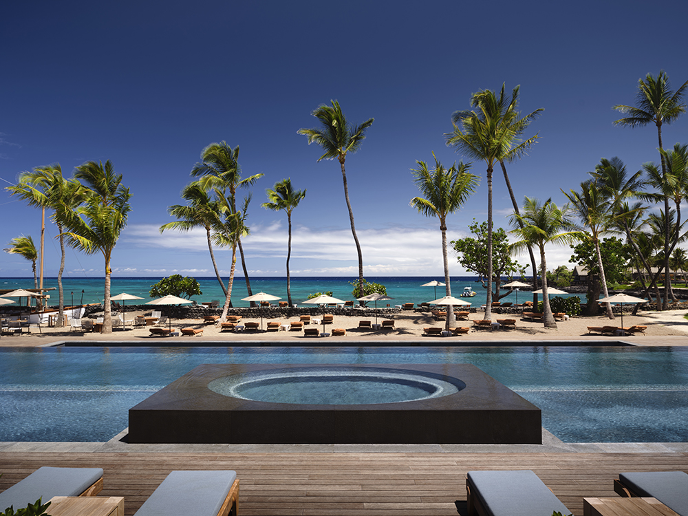 Infinity-edge pool overlooking a white sand beach with palm trees and turquoise ocean at Kona Village, a Rosewood Resort on the Kohala Coast, Hawaii — a Three Michelin Key hotel offering luxury beachfront accommodations and world-class service.