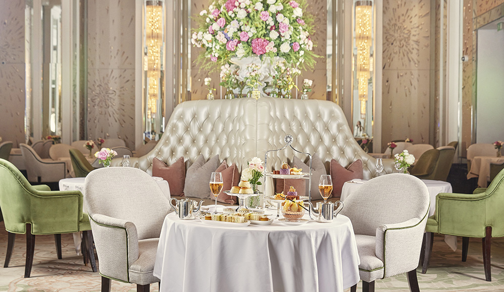 Round table set for afternoon tea with tiered pastries, champagne glasses, and flowers in The Langham London