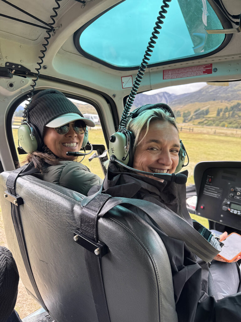 Two smiling Inspirato members seated in a helicopter, wearing headsets and ready for a scenic flight near Queenstown, New Zealand.