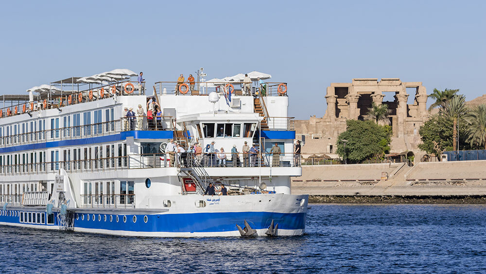 Oberoi Philae luxury Nile river cruise ship sailing past ancient temple ruins along the Nile River in Egypt.
