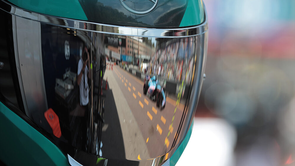 Close-up of a Mercedes team helmet visor reflecting a Formula One car on the Monaco Grand Prix street circuit.