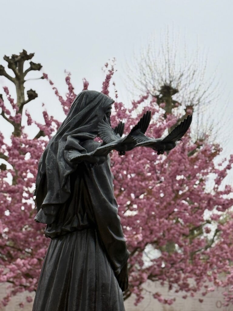 A bronze statue with pink blooms on trees in the background