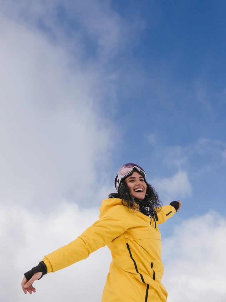 a woman smiling in a yellow winter coat against a blue sky